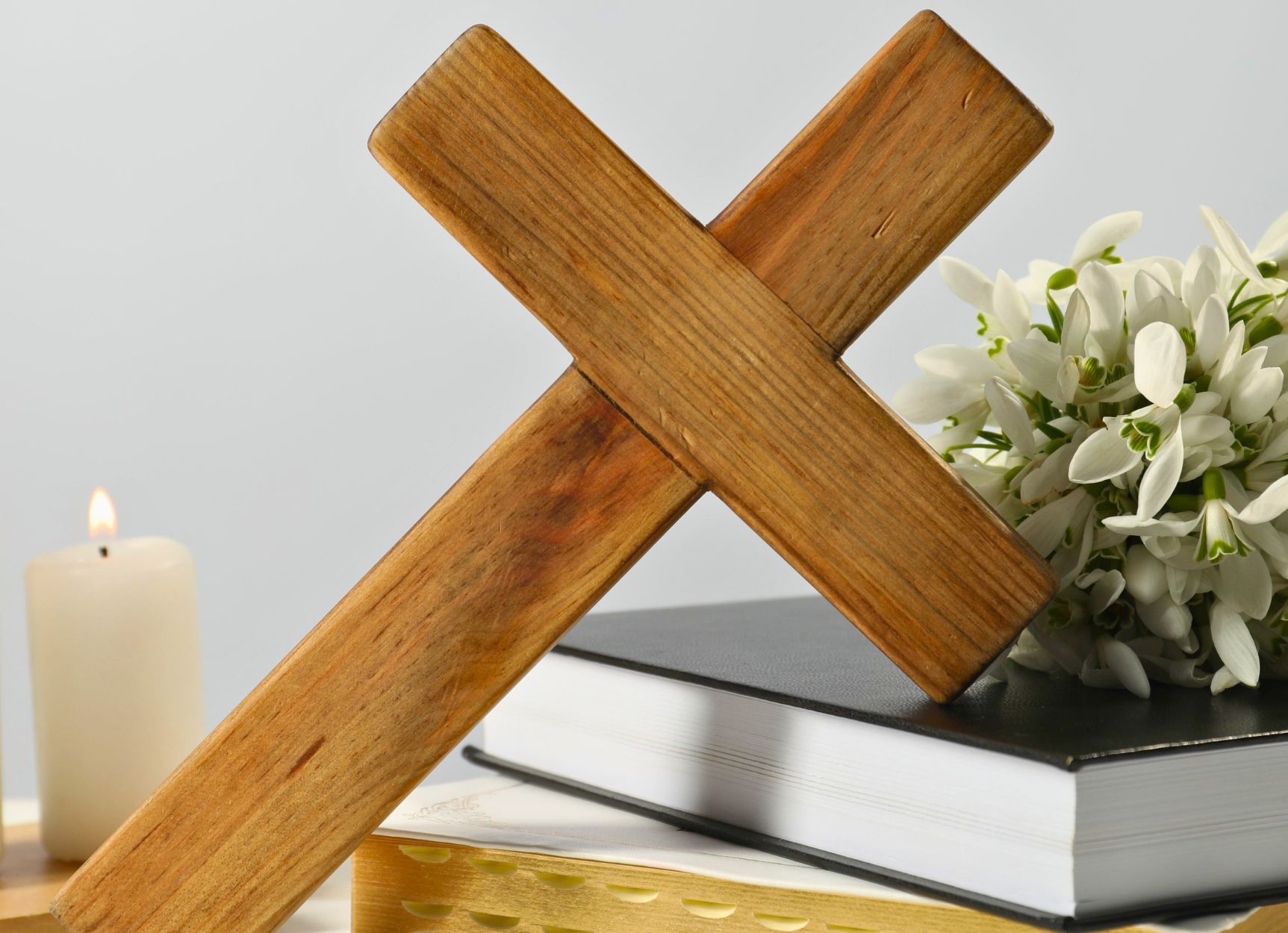 Wooden cross resting on books with white lilies, symbolizing faith and education in natural wellness